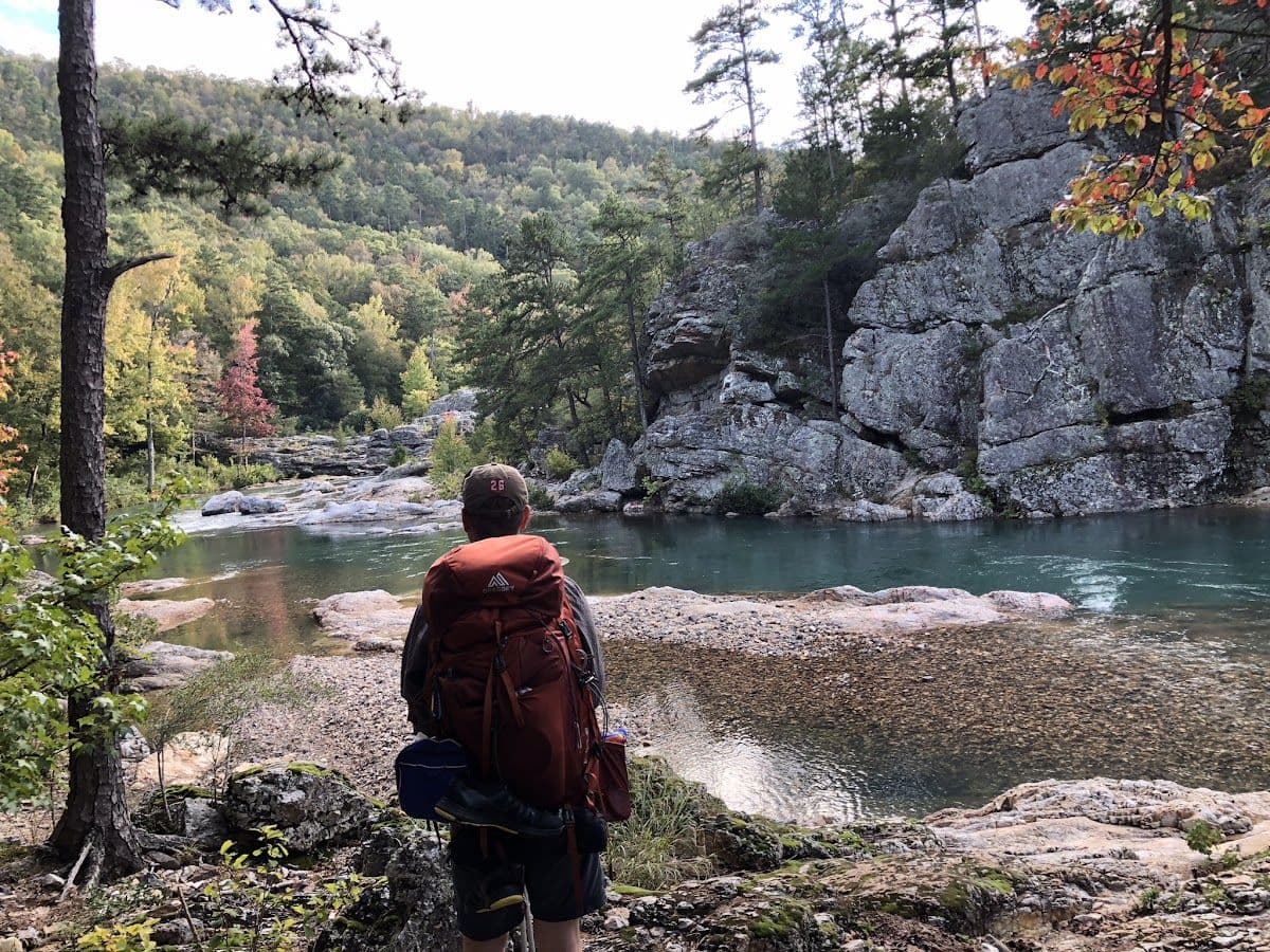 Backpacker overlooking blue-green water beneath Ozark bluffs